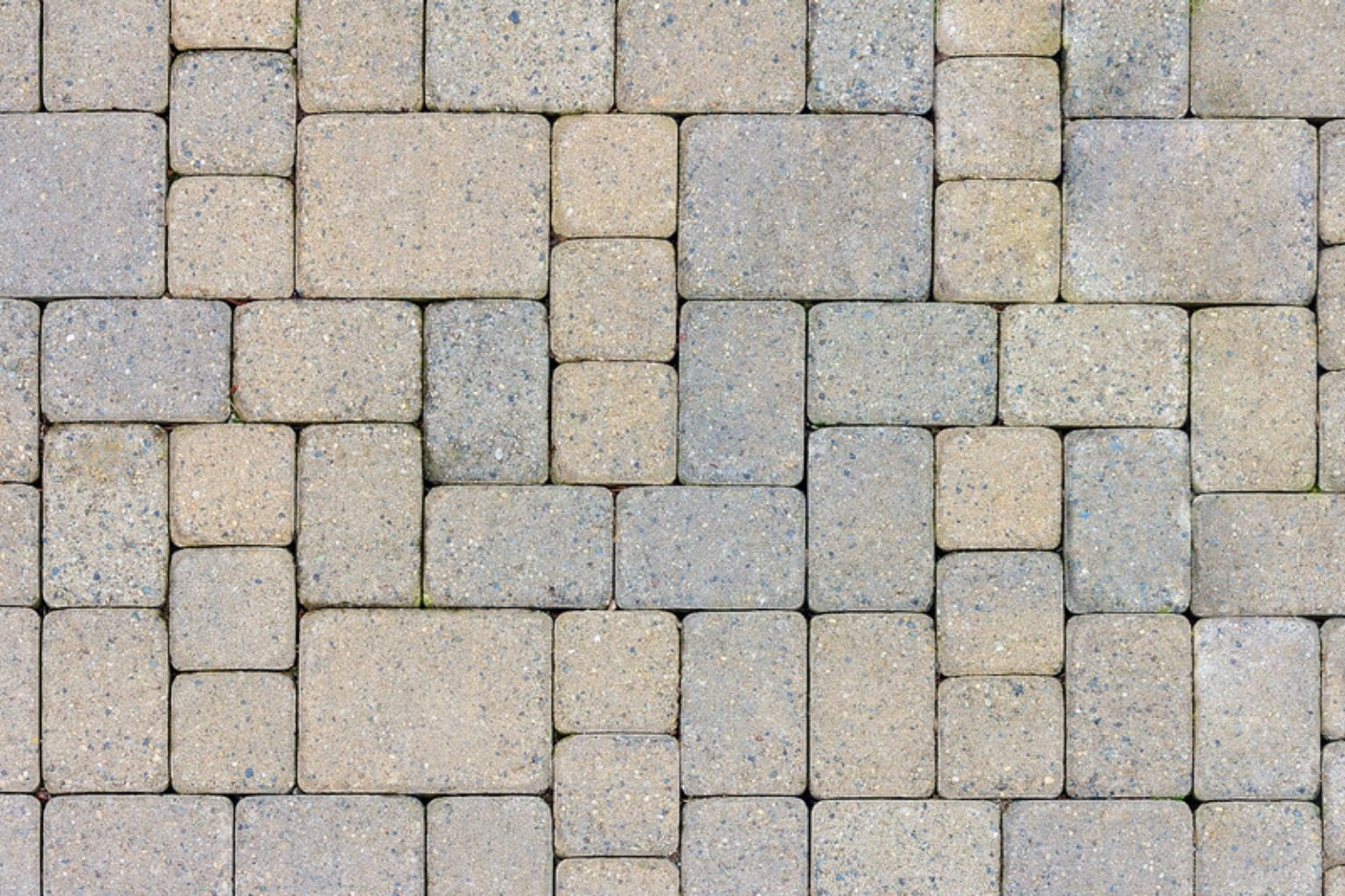 Lyse betonbelægningssten i varierende størrelser lagt i et gitter, set ovenfra