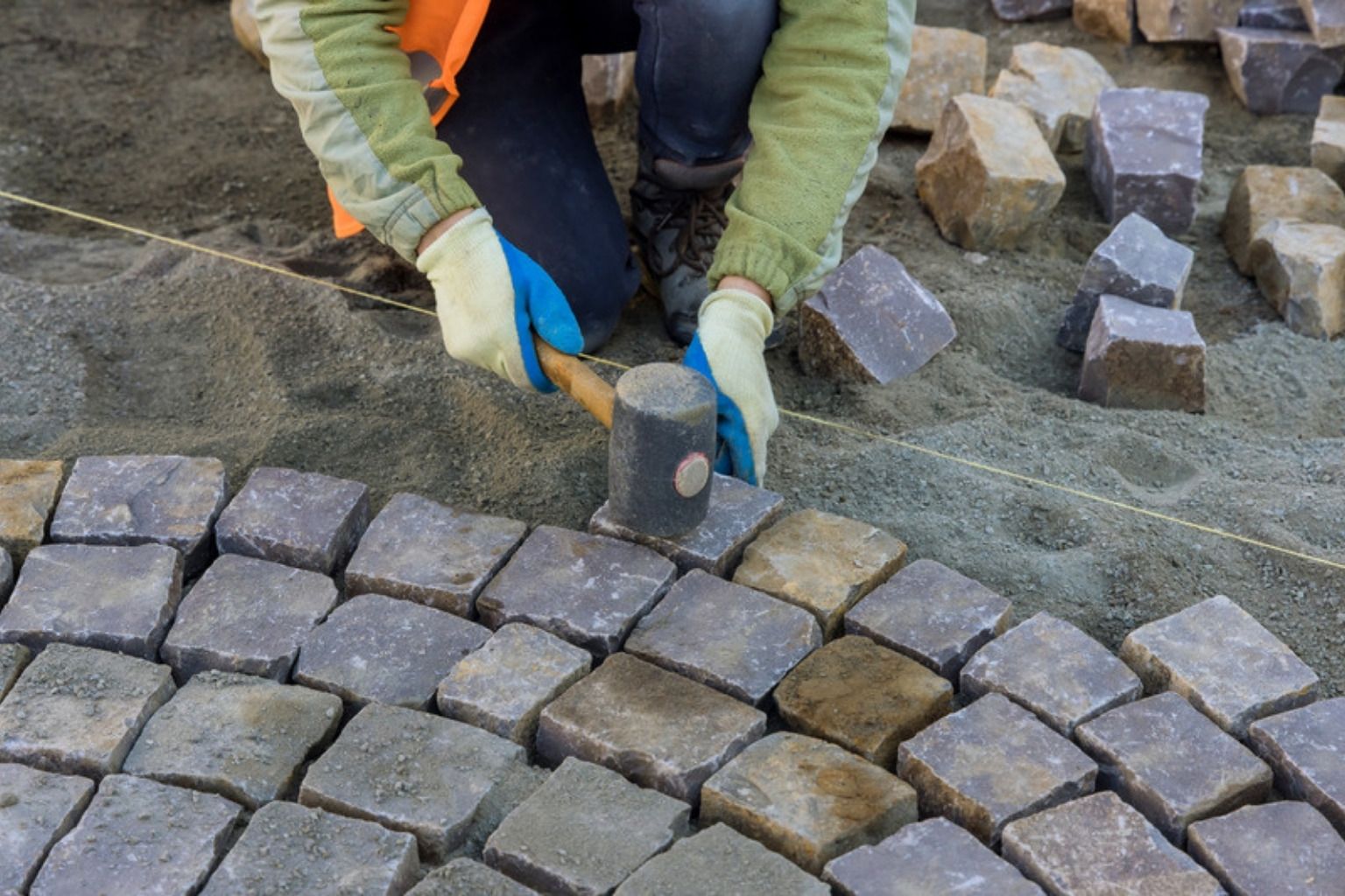 Håndværker lægger brosten i buer og banker dem på plads med hammer