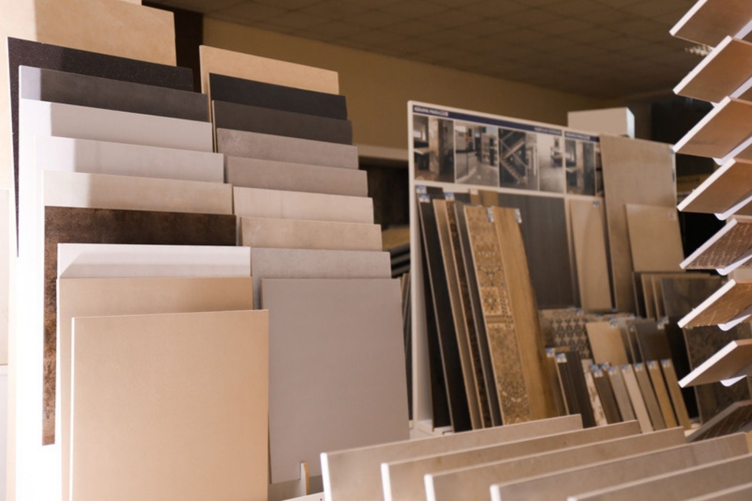 Store keramiske gulvfliser i grå og beige nuancer stillet op i stativer i en flisebutik